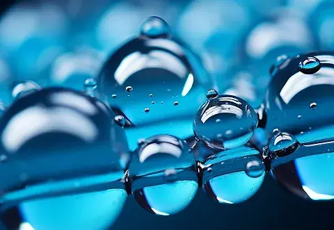 Close-up view of several translucent water droplets on a smooth blue surface, with reflections visible on the droplets.
