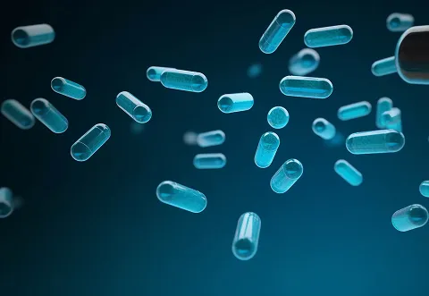 Blue translucent capsules floating against a dark blue background, some with visible white powder inside, suggesting medication or supplements.