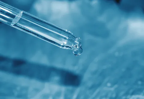 A close-up of a glass dropper releasing a single droplet of liquid, set against a blurred blue background.